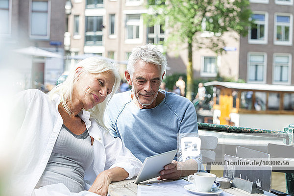 Netherlands  Amsterdam  senior couple with digital tablet in an outdoor cafe