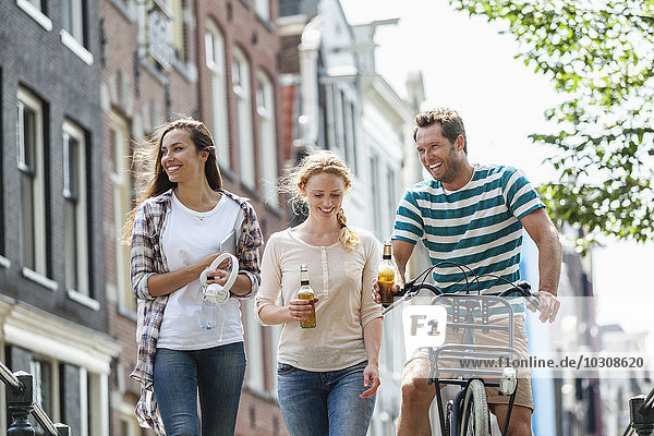 Niederlande  Amsterdam  glückliche Freunde mit Bierflaschen und Fahrrad in der Stadt
