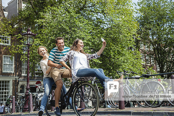 Netherlands  Amsterdam  three playful friends riding on one bicycle in the city