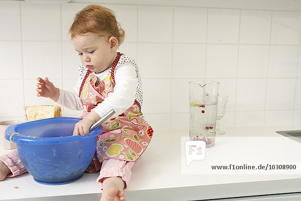 Kleines Mädchen sitzt auf der Küchentheke mit Rührschüssel