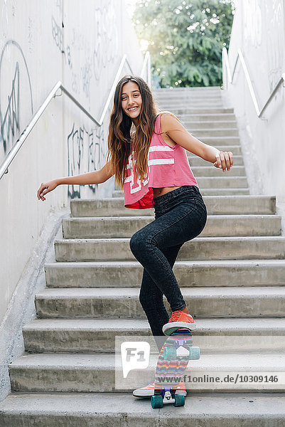 Fröhliches Teenagermädchen mit Skateboard auf der Treppe