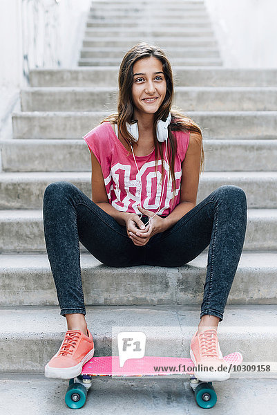 Portrait of teenage girl sitting on stairs with a skateboard and headphones