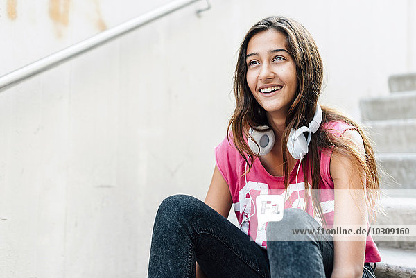 Portrait of smiling teenage girl with headphones sitting on stairs