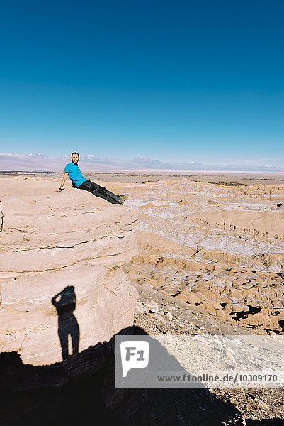 Chile  Atacama-Wüste  Mann auf einer Klippe sitzend mit Schatten eines Fotografen