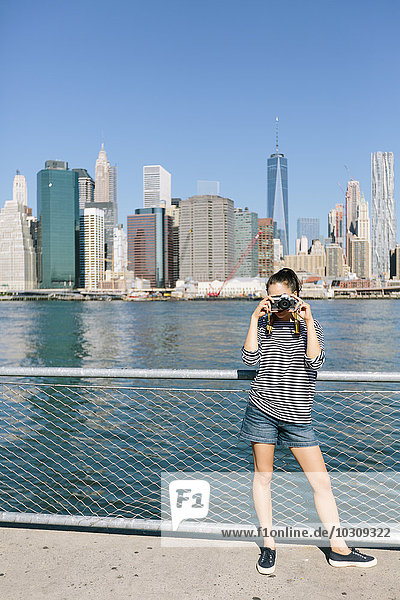 USA  New York City  junge Frau fotografiert mit Kamera vor der Skyline