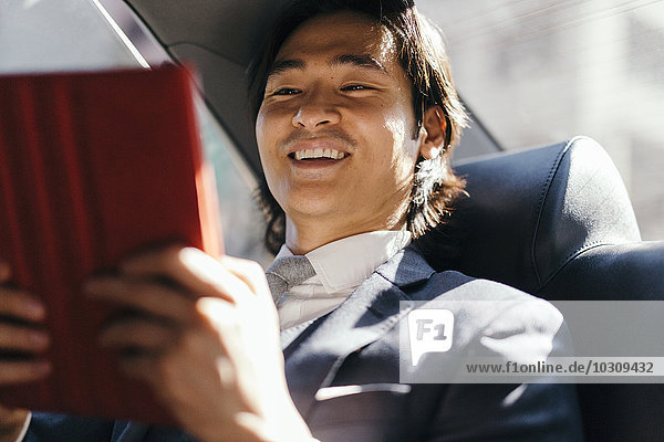 Lächelnder Geschäftsmann auf dem Rücksitz eines Autos mit digitalem Tablett