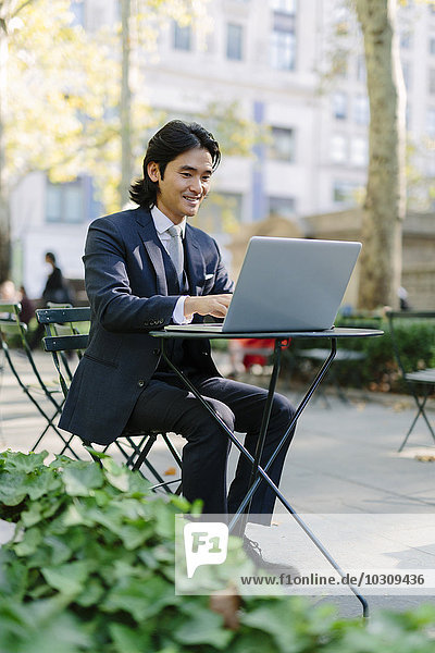 USA  New York City  Manhattan  smiling businessman working with a laptop in Bryant Park