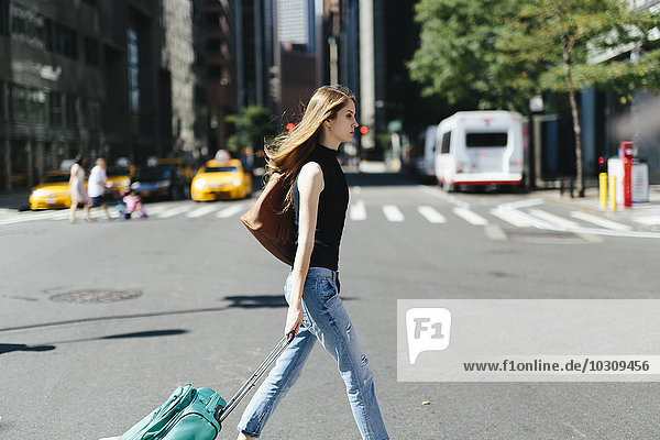 USA  New York City  young woman with rolling suitcase crossing a street