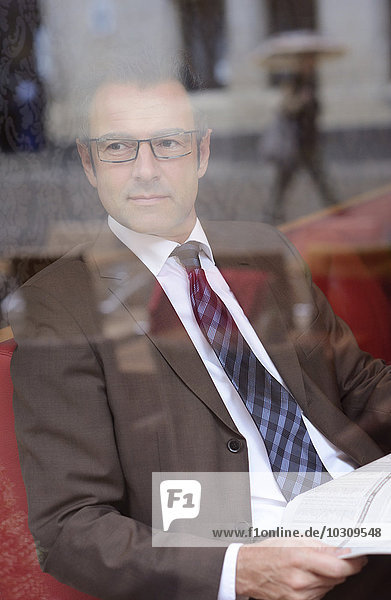 Ein Geschäftsmann sitzt in einem Café mit einer Zeitung und schaut sich etwas an.