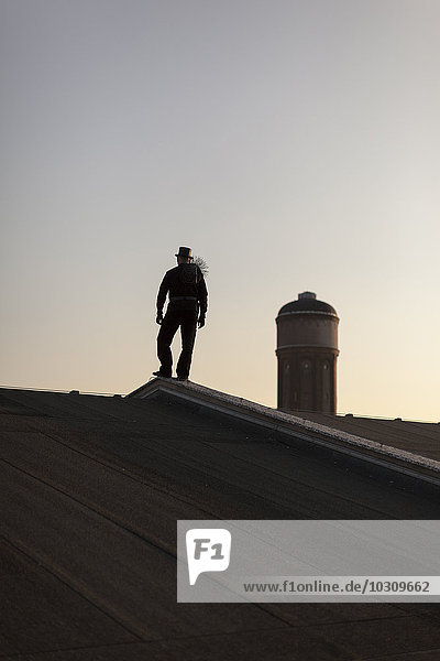 Germany  silhouette of chimney sweep standing on rooftop at twilight