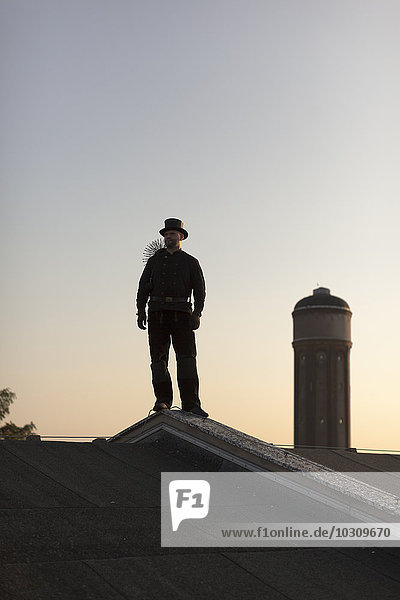 Germany  chimney sweep standing on rooftop at twilight
