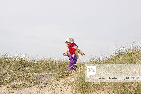 Glückliches kleines Mädchen  das auf einer Stranddüne läuft