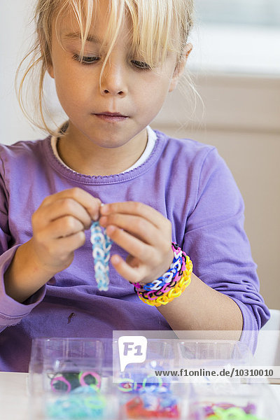 Porträt des kleinen Mädchens  das Webstuhlarmbänder herstellt