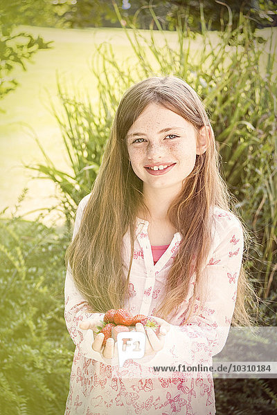 Porträt eines lächelnden Mädchens mit einer Handvoll Erdbeeren