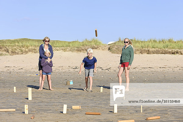 Mutter und drei Kinder spielen Kubb am Strand