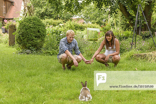 Junges Paar erwartet Baby  hockt im Garten  beobachtet Hase