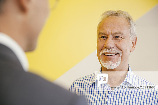 Porträt eines lächelnden älteren Mannes  der mit einem anderen Mann im Büro spricht.