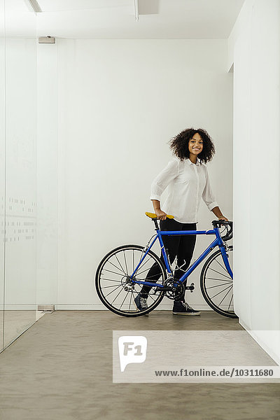 Smiling young woman with bicycle in office
