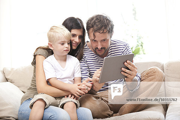 Parents and little son sitting on the couch with digital tablet