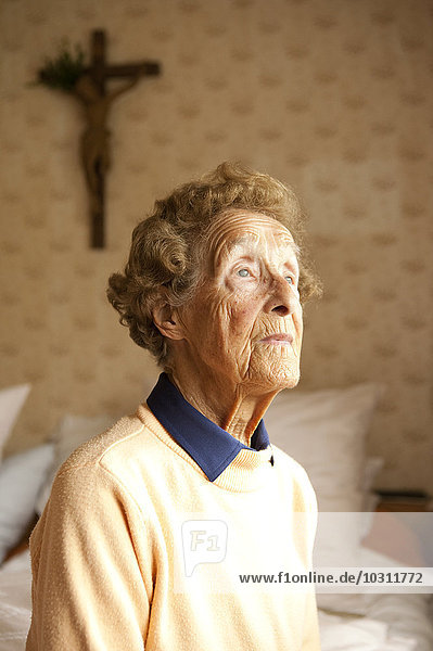 Porträt einer alten Frau  die in ihrem Schlafzimmer auf dem Bett sitzt.