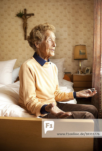 Porträt einer alten Frau  die in ihrem Zimmer auf dem Bett sitzt.