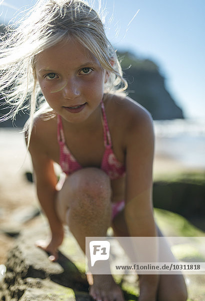 Porträt eines kleinen Mädchens  das auf einen Felsen am Strand klettert.