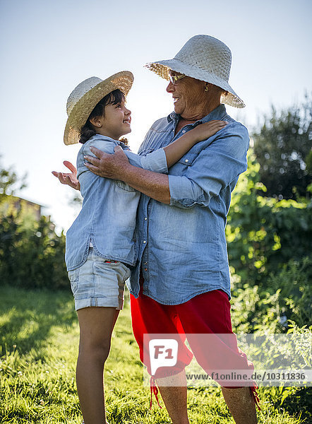 Seniorin umarmt ihre Enkelin im Garten