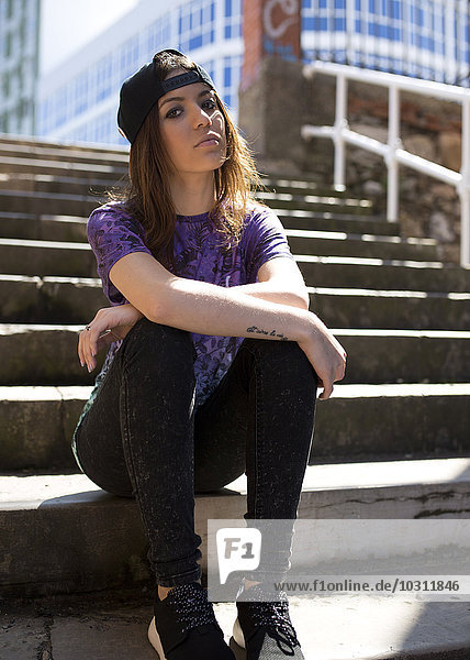 Portrait of young woman with baseball cap sitting on stairs