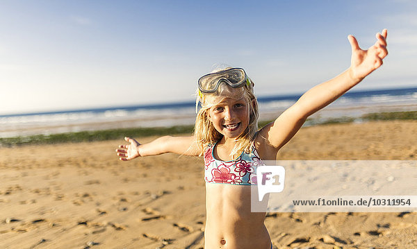 Spanien  Colunga  Porträt des lächelnden blonden Mädchens mit Tauchermaske und ausgestreckten Armen am Strand
