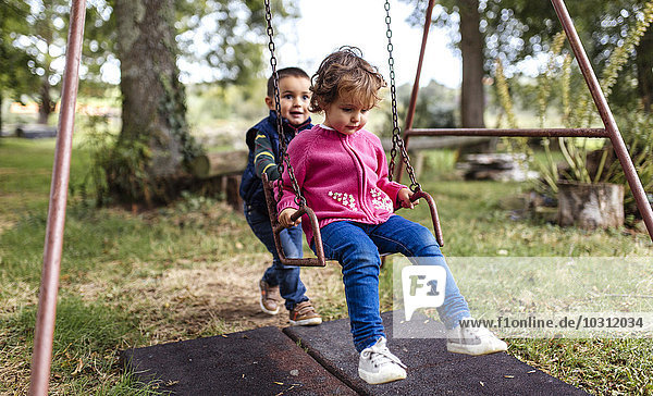 Two little children playing with swing in a garden