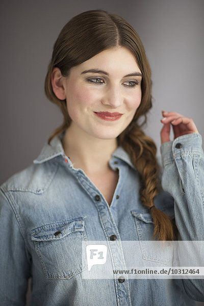 Porträt einer lächelnden jungen Frau mit Zopf im Jeanshemd