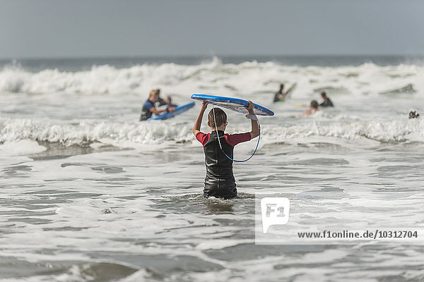 Junge trägt Surfbrett ins Meer