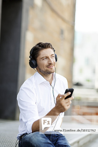 Portrait of smiling man hearing music with MP3 Player and headphones