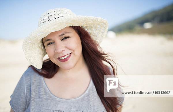 Porträt einer lächelnden Frau mit Hut am Strand