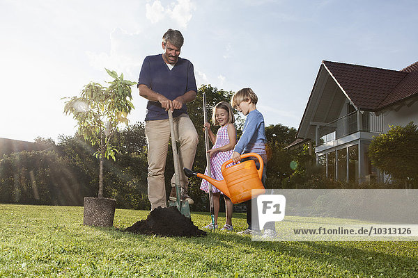 Father and children planting tree in garden