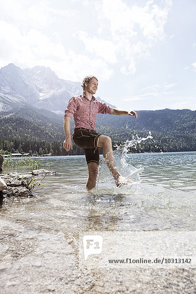 Deutschland  Bayern  Eibsee  glücklicher Mann in Lederhose  der ins Wasser spritzt