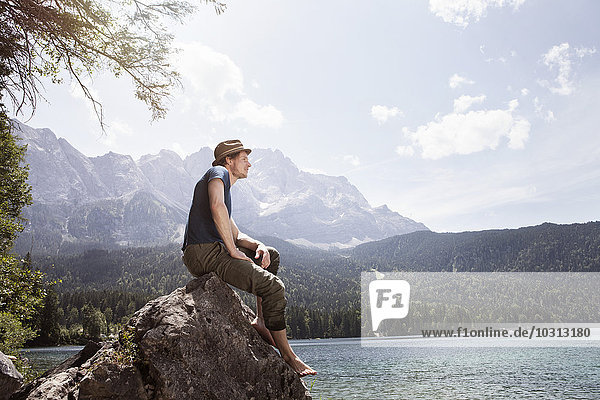 Germany  Bavaria  Eibsee  man sitting on rock on lakeshore