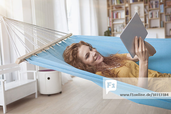 Lächelnde Frau zu Hause in der Hängematte liegend mit digitalem Tablett