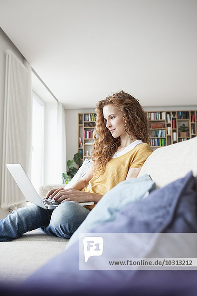 Woman at home sitting on couch using laptop