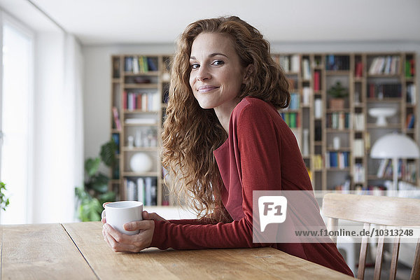 Lächelnde Frau zu Hause sitzend am Holztisch mit Tasse