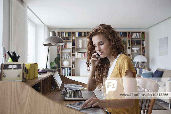Frau zu Hause mit Handy  digitalem Tablett und Laptop auf dem Sekretärinnenschreibtisch