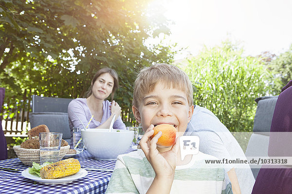 Lächelnder Junge mit seiner Familie  die eine Frucht am Gartentisch hält.