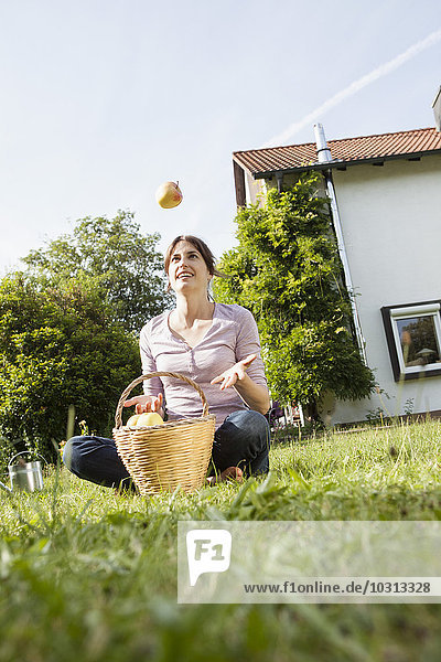 Lächelnde Frau sitzt im Garten und kotzt den Apfel.