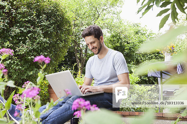 Mann im Garten sitzend mit Laptop