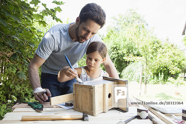 Vater und Tochter malen ein Vogelhaus