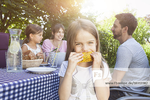 Mädchen beim Essen eines Maiskolbens auf einem Familiengrill im Garten