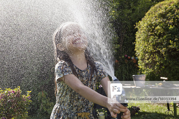 Mädchen spritzt mit Wasser im Garten