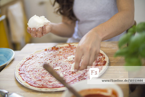 Junge Frau legt Mozzarella auf Pizza