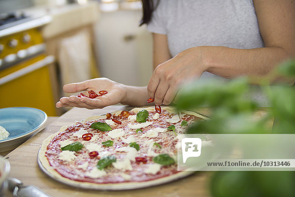 Young woman preparing pizza with mozzarella  chili peppers and basil