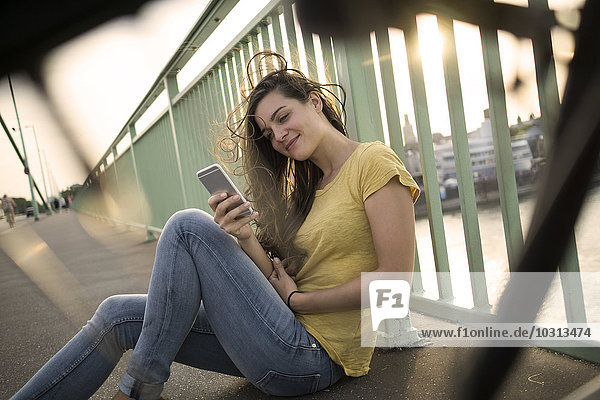 Deutschland  Köln  Frau auf der Rheinbrücke mit Blick auf ihr Smartphone